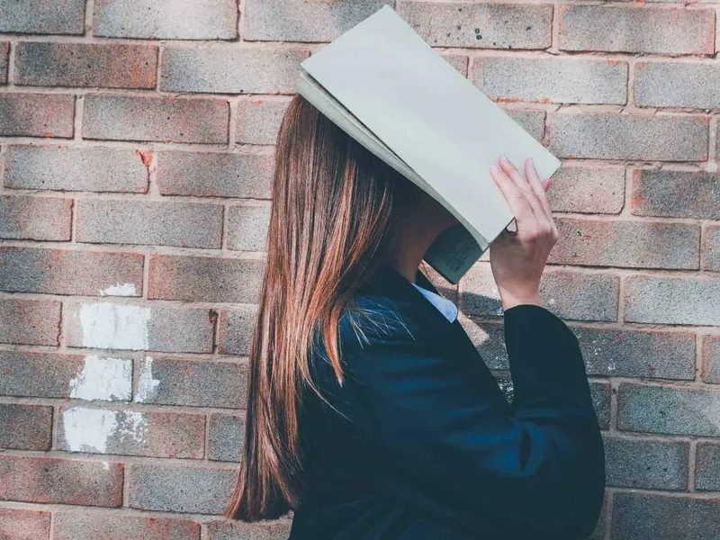 Scoolgirl hiding her face behind a book