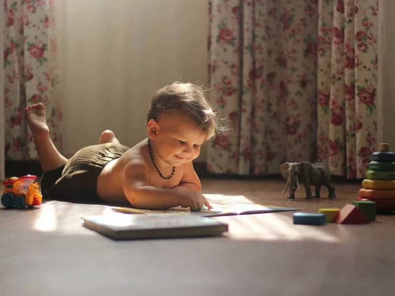 Baby looking at book and surrounded by toys