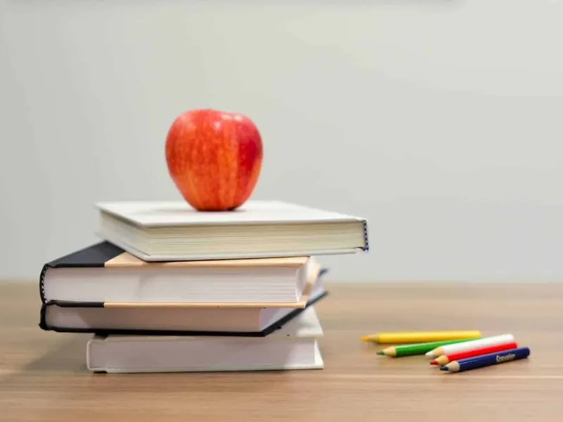 Pile of books with an apple on top next to some coloured pencils